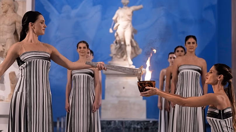 La grande prêtresse Mary Mina, à gauche, allume une torche de la flamme olympique lors de la cérémonie au musée archéologique d'Olympie, le 26 novembre 2025.