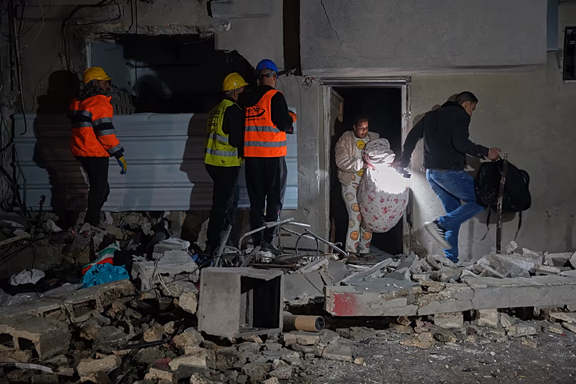Des habitants transportent leurs effets personnels alors qu'ils quittent un bâtiment endommagé par une frappe de missile à Tel Aviv, en Israël, le samedi 28 mars 2026.