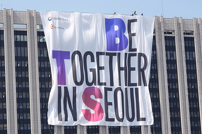 Les travailleurs accrochent une banderole faisant la promotion du concert de retour des BTS sur un bâtiment gouvernemental près de la place Gwanghwamun.