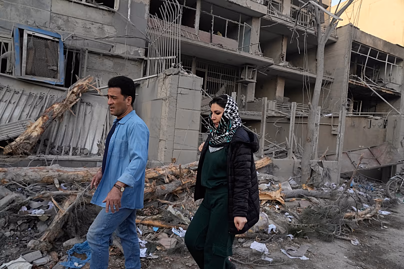Des gens passent devant des bâtiments endommagés lors d’une frappe contre un commissariat de police lors d’attaques militaires conjointes américano-israéliennes en cours à Téhéran, en Iran, le 2 mars 2026.