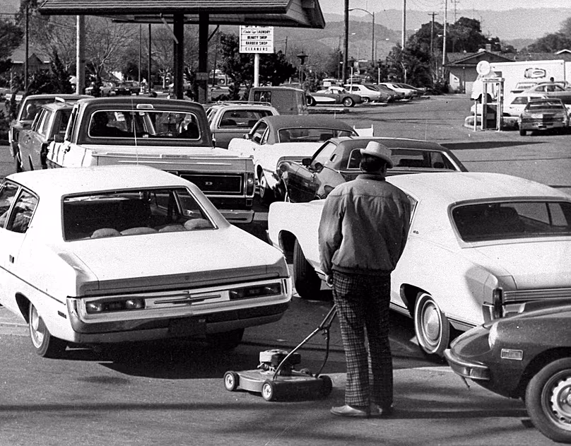 DÉPOSER. Des conducteurs et un homme poussant une tondeuse à gazon font la queue dans une station-service pendant l'embargo pétrolier arabe, San Jose, Californie, mars 1974.