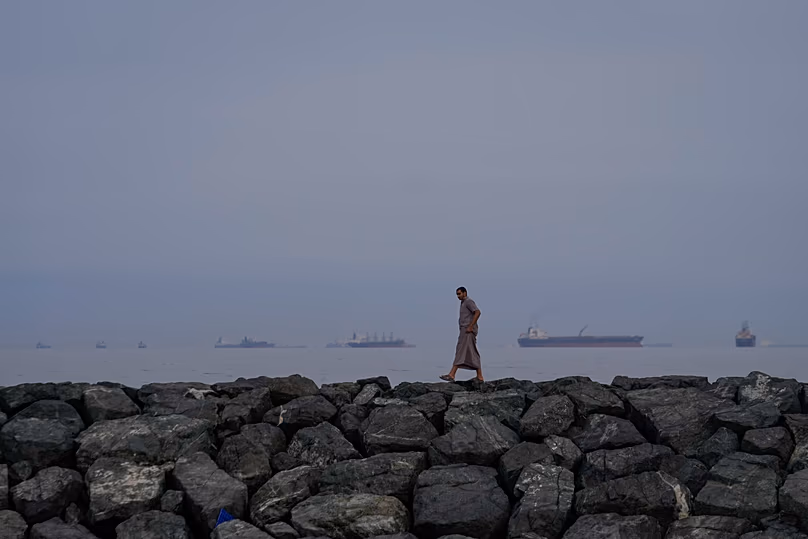 Un homme marche le long du rivage alors que des pétroliers et des cargos font la queue dans le détroit d'Ormuz, le 11 mars 2026.