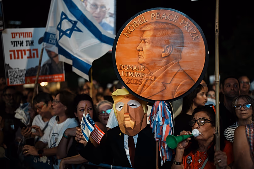 Un homme portant un masque ressemblant au président américain Donald Trump tient une pancarte en forme de médaille du prix Nobel de la paix lors d'un rassemblement à Tel Aviv, le 11 octobre 2025.