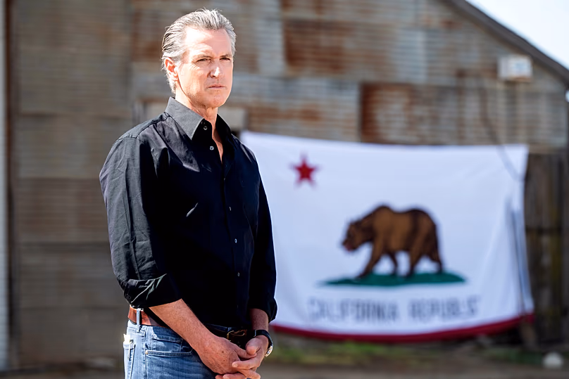 Le gouverneur sortant de Californie, Gavin Newsom, se tient devant un drapeau de l'État. (Photo AP/Noé Berger)