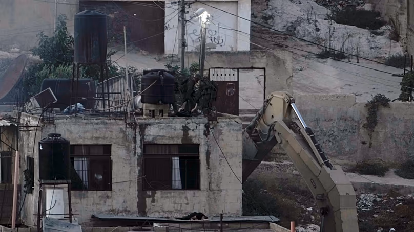 Des soldats israéliens regardent par-dessus un toit où deux personnes gisent immobiles dans la ville de Qabatiya en Cisjordanie lors d'un raid, le jeudi 19 septembre 2024. (AP Photo/Majdi Mohammed)