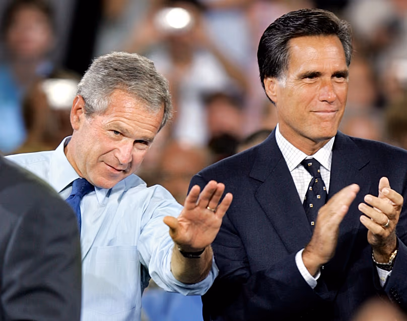 Le président américain George W. Bush salue tandis que le gouverneur du Massachusetts, Mitt Romney, applaudit lors d'un événement de campagne à Nashua, New Hampshire, le 30 août 2004 (AP Photo/Steven Senne, File)