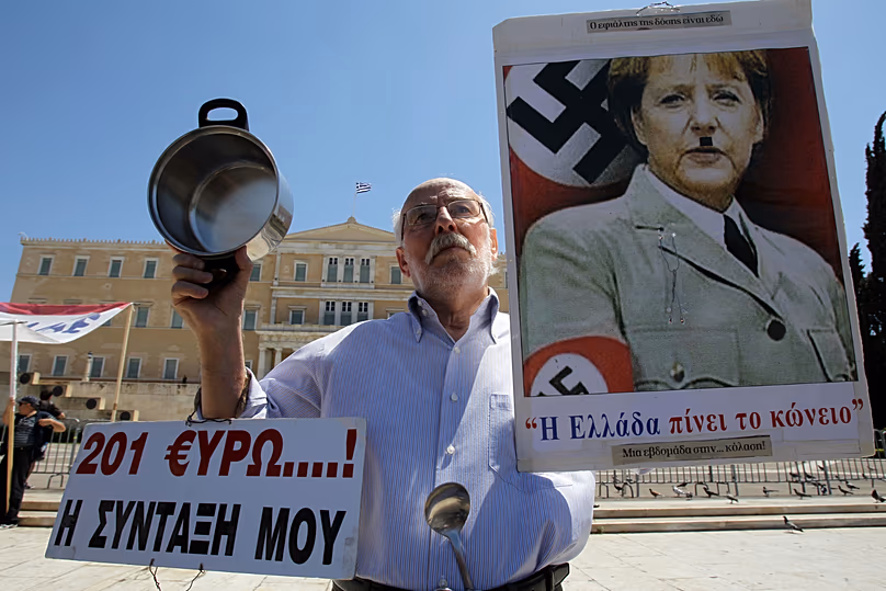Un homme âgé tient une affiche avec une photo de la chancelière allemande Angela Merkel, ressemblant à Adolf Hitler lors d'une manifestation à Athènes. 1er mai 2013 (Photo AP/Thanassis)