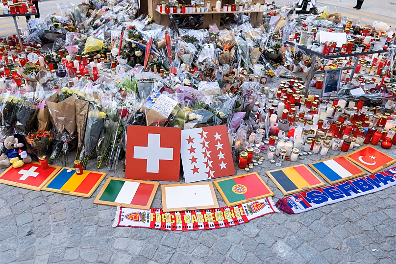 Des plaques arborant des drapeaux internationaux côtoient des fleurs et des bougies au bar "Le Constellation" à Crans-Montana, le 6 janvier 2026