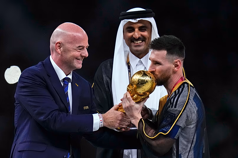 DOSSIER – L'Argentin Lionel Messi embrasse le trophée présenté par le président de la FIFA Gianni Infantino, à gauche, sous le regard de l'émir du Qatar, Cheikh Tamim bin Hamad Al Thani.