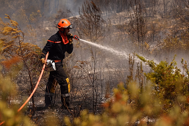 Un pompier pulvérise de l'eau sur de la végétation et des arbres brûlés lors d'opérations de nettoyage dans une zone touchée par un incendie de forêt à Cotignac, en France, le mercredi 22 juillet 2026.