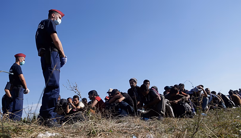 Un groupe de migrants est assis et attend d'être escorté jusqu'à un train après avoir traversé une frontière croate près du village de Zakany, en Hongrie, le mercredi 23 septembre 2015.