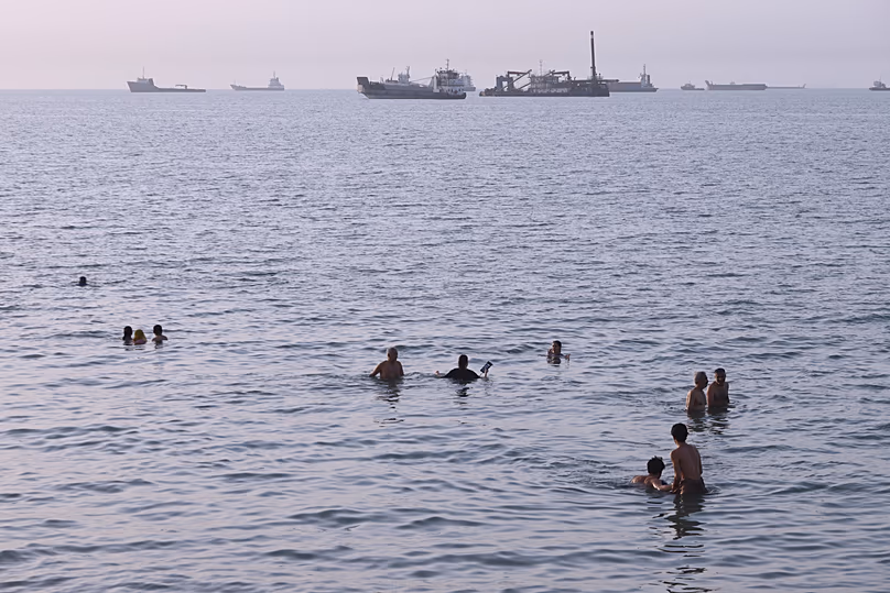Des habitants nagent alors que des cargos et des navires commerciaux sont ancrés dans le détroit d'Ormuz, au large de Bandar Abbas, le 6 août 2026.