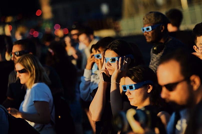 Des gens utilisent des lunettes pour éclipse solaire pour regarder le soleil lors d'une éclipse solaire à Berlin, le 12 août 2026.