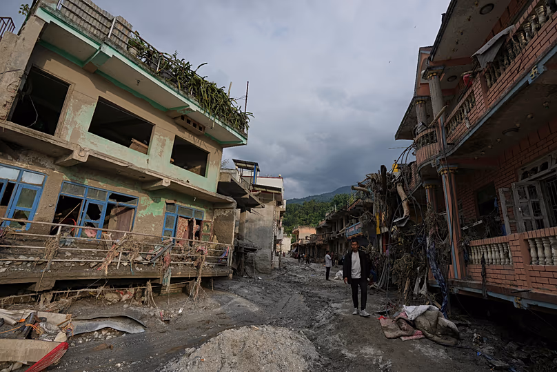 Des gens marchent le long d'une rue bordée de structures endommagées après des crues soudaines dans la région de Devighat, dans le district de Nuwakot, au Népal, le 28 août 2026.