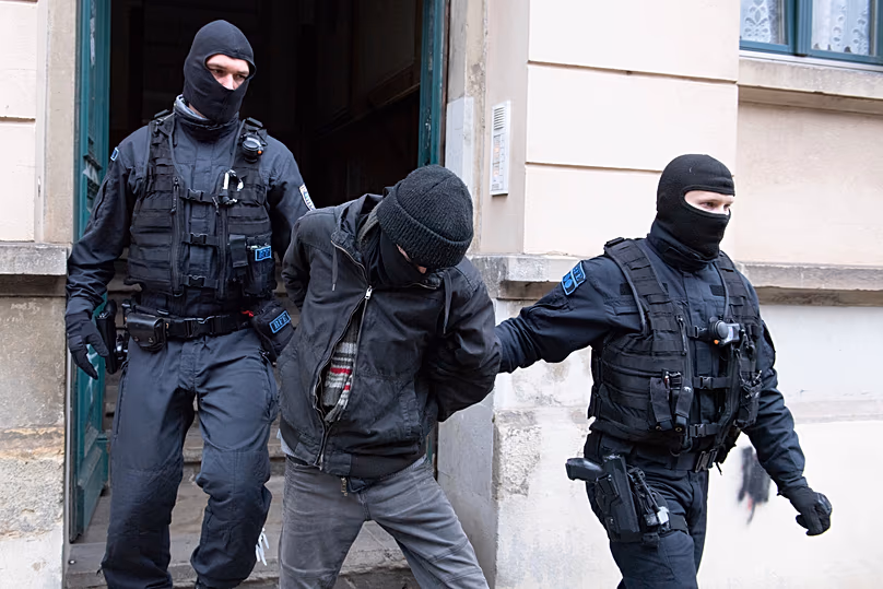 Des policiers conduisent un suspect hors de l'entrée d'un immeuble lors d'un raid dans le quartier de Pieschen à Dresde, le 15 décembre 2021.
