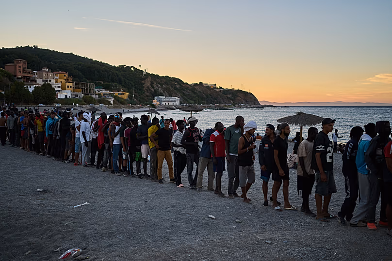 Des migrants arrivés du Maroc vers l'Espagne font la queue pour une distribution de nourriture sur une plage du territoire espagnol de Ceuta, le 3 août 2026.