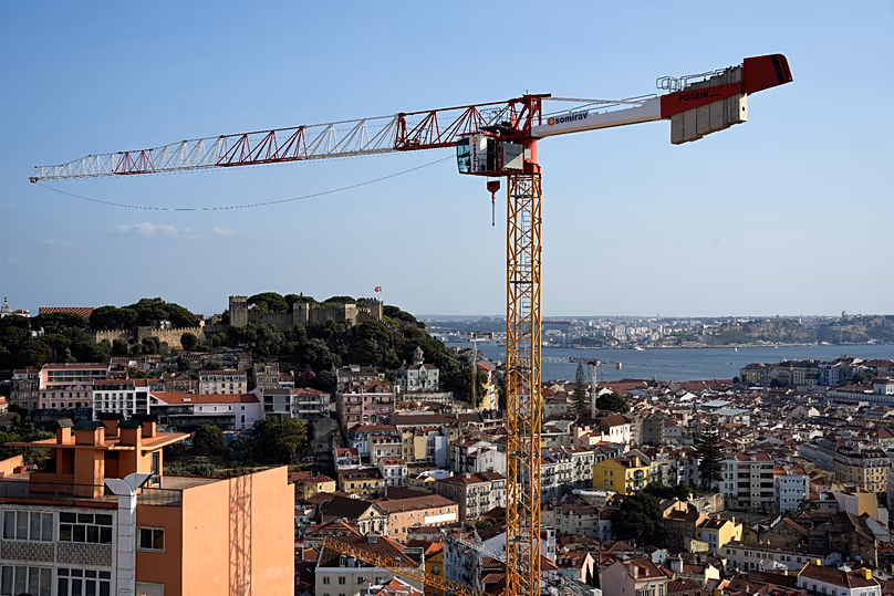 Une grue s'élève au-dessus des bâtiments, avec le château Saint-Georges et le Tage en arrière-plan, à Lisbonne