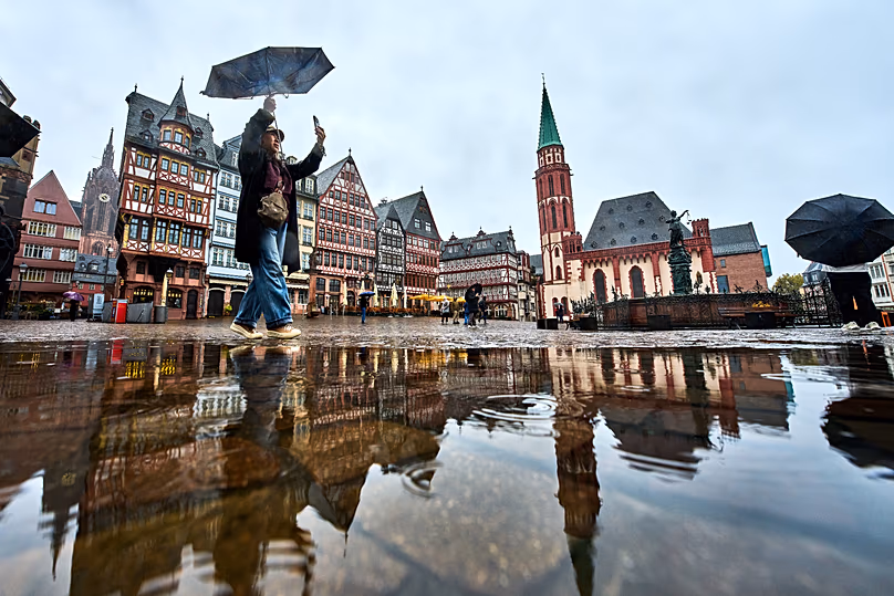 Un touriste prend des photos sur la place Roemerberg à Francfort, en Allemagne, sous la pluie, le dimanche 25 octobre 2026. (AP Photo/Michael Probst)